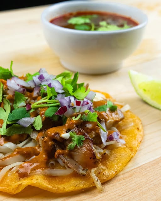 Taco birria garni de coriandre et d’oignons, servi avec son consommé